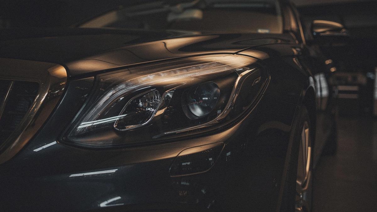 Close crop of a polished headlight and front wing on a dark luxury car